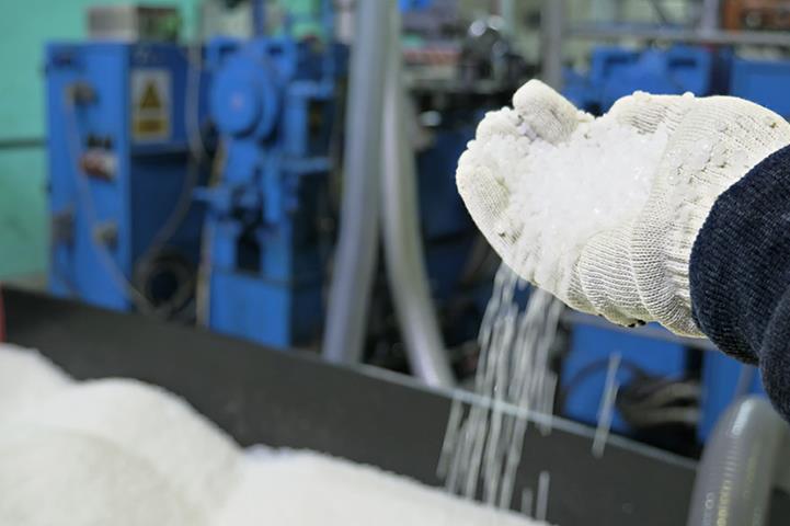 gloved hand over open container filled with plastic granules