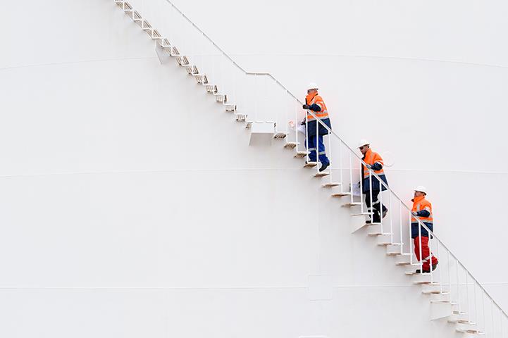three men in orange and wearing hardhats climbing storage tank stairs