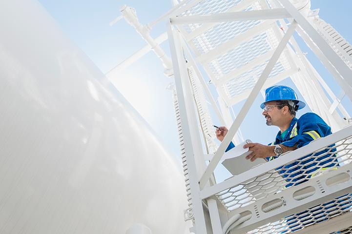 worker on platform checking exterior of white tanks